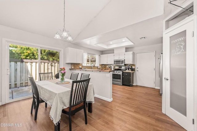 dining area with a raised ceiling, lofted ceiling, a notable chandelier, and light hardwood / wood-style flooring