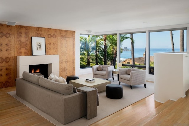 living room with wooden walls, light wood-type flooring, a water view, and floor to ceiling windows