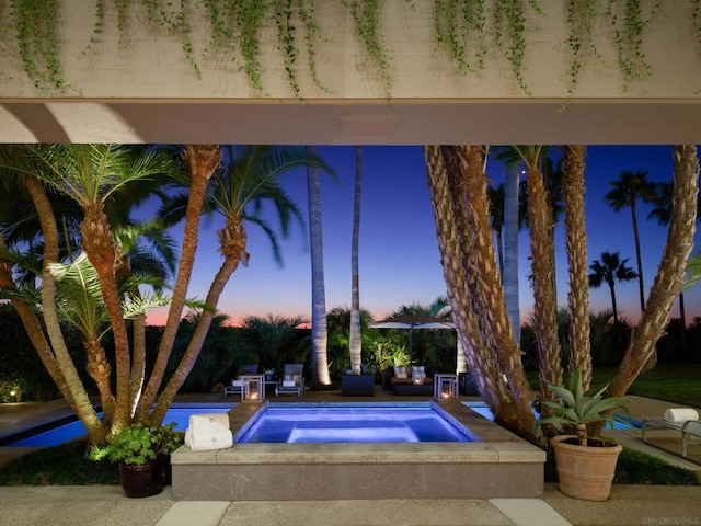 pool at dusk featuring an in ground hot tub