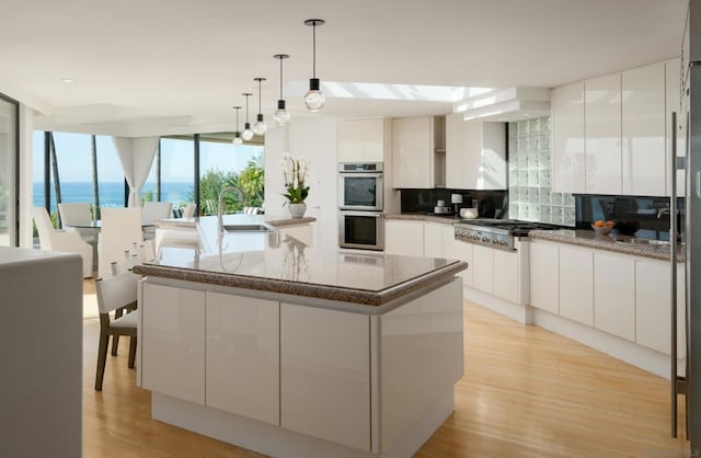 kitchen with appliances with stainless steel finishes, decorative backsplash, white cabinets, a kitchen island, and a water view