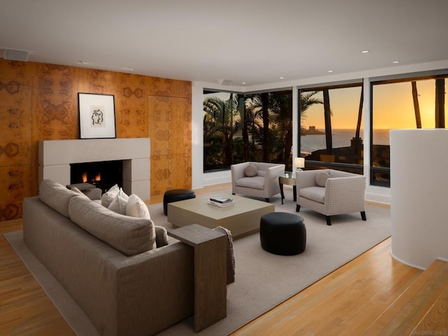 living room featuring expansive windows, a water view, a tile fireplace, and wood-type flooring