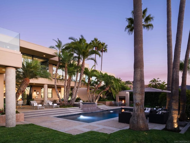 pool at dusk with an outdoor living space with a fireplace and a patio