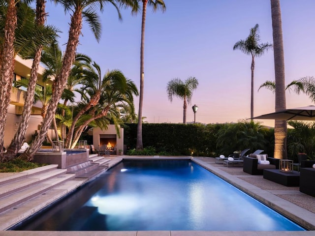 pool at dusk featuring a patio area and an outdoor living space with a fireplace