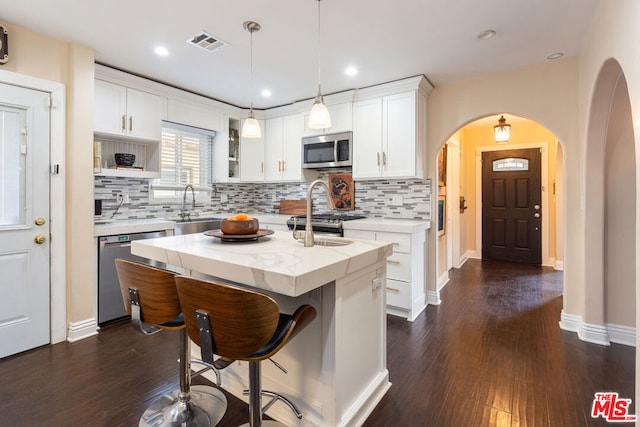 kitchen featuring appliances with stainless steel finishes, a kitchen island with sink, white cabinets, sink, and light stone counters