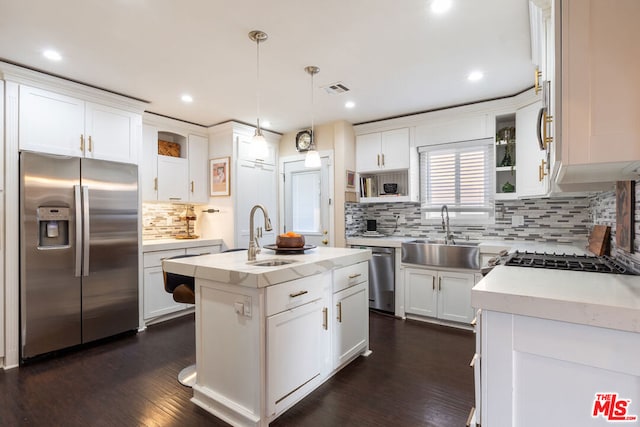 kitchen featuring appliances with stainless steel finishes, sink, white cabinets, pendant lighting, and a center island with sink