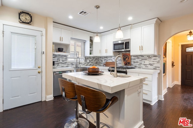 kitchen with white cabinets, backsplash, appliances with stainless steel finishes, and a center island with sink