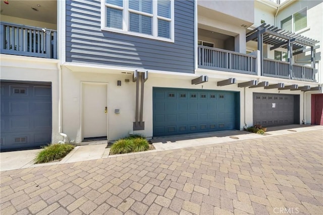 exterior space with decorative driveway, a balcony, an attached garage, and stucco siding