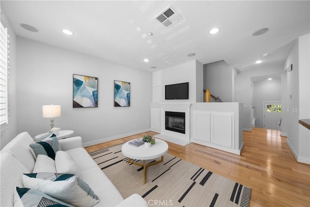 living room featuring recessed lighting, visible vents, light wood-style flooring, a glass covered fireplace, and baseboards