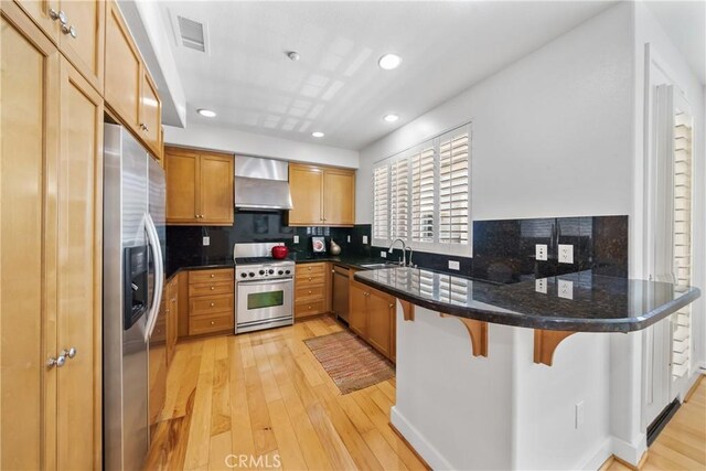 kitchen featuring a kitchen breakfast bar, wall chimney range hood, sink, kitchen peninsula, and stainless steel appliances