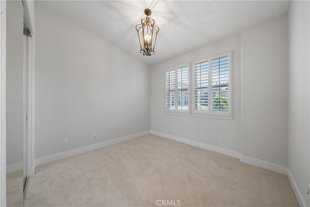 spare room featuring light colored carpet, a notable chandelier, and baseboards