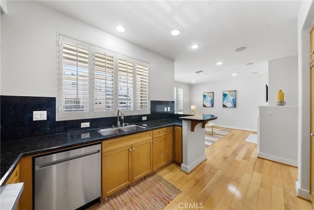 kitchen with brown cabinetry, a peninsula, stainless steel dishwasher, light wood-style floors, and a sink