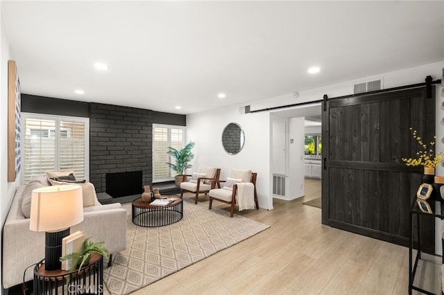 living room featuring a brick fireplace, light hardwood / wood-style floors, a wealth of natural light, and a barn door