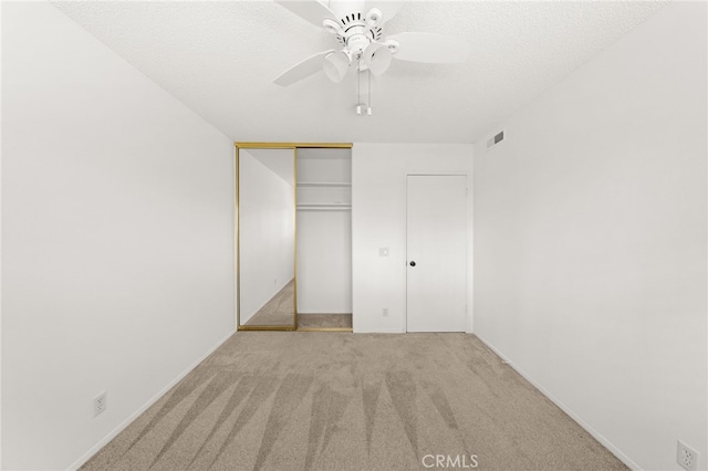 unfurnished bedroom featuring a textured ceiling, light colored carpet, a closet, and ceiling fan