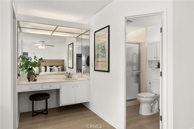 bathroom featuring ceiling fan, hardwood / wood-style flooring, toilet, walk in shower, and vanity