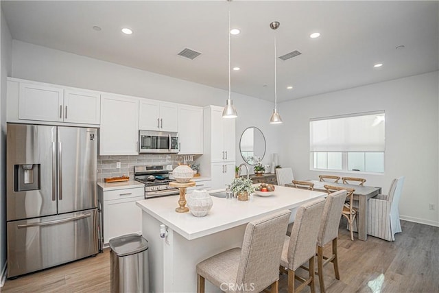 kitchen with white cabinets, appliances with stainless steel finishes, sink, hanging light fixtures, and a kitchen island with sink