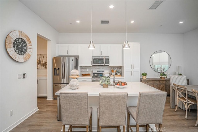 kitchen featuring white cabinets, stainless steel appliances, decorative backsplash, hanging light fixtures, and a kitchen island with sink