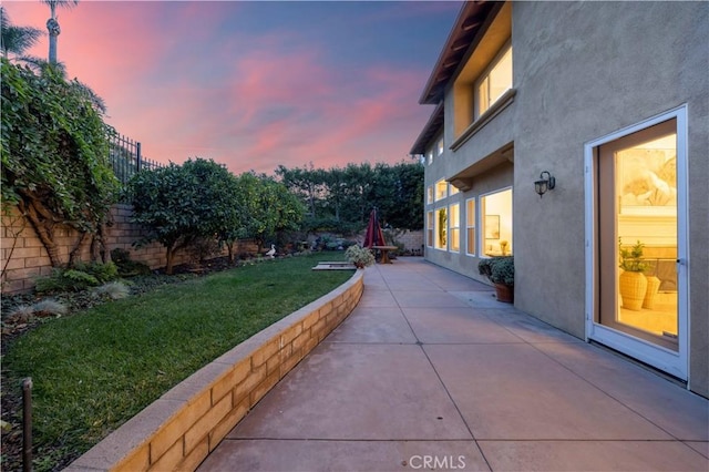 patio terrace at dusk featuring a fenced backyard and a yard