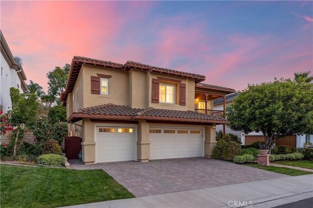 mediterranean / spanish-style house featuring a garage, a balcony, a tiled roof, decorative driveway, and stucco siding