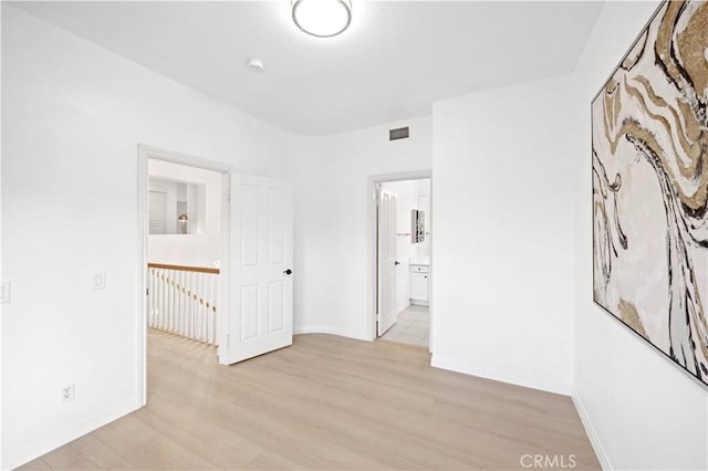 unfurnished bedroom with light wood-type flooring, visible vents, connected bathroom, and baseboards