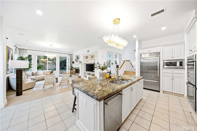 kitchen with an inviting chandelier, open floor plan, white cabinetry, a kitchen island with sink, and built in appliances