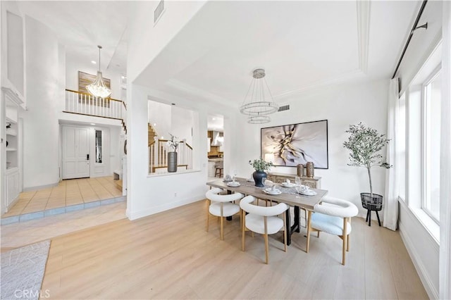 dining space featuring stairway, a tray ceiling, light wood-style flooring, and an inviting chandelier