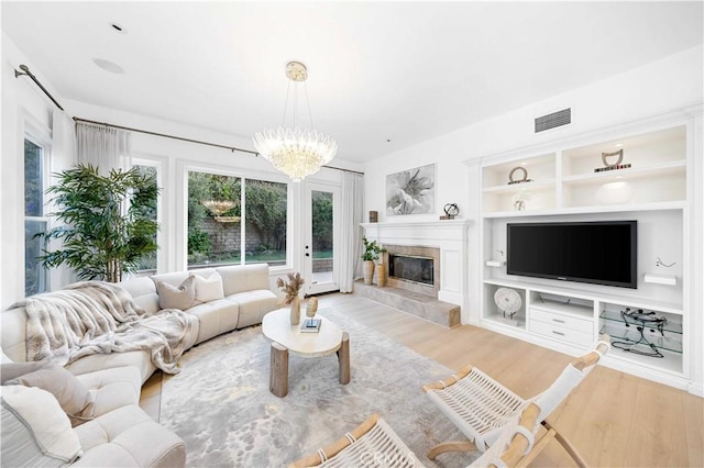 living room featuring a tiled fireplace, a notable chandelier, built in features, and light hardwood / wood-style floors