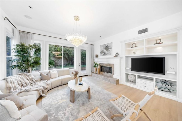 living area featuring built in shelves, light wood-style flooring, visible vents, a tiled fireplace, and an inviting chandelier