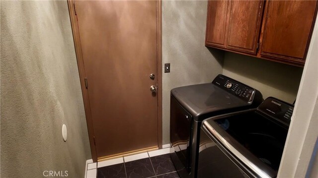 washroom with dark tile patterned flooring, washing machine and dryer, and cabinets