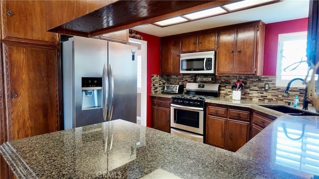 kitchen featuring sink, dark stone countertops, kitchen peninsula, stainless steel appliances, and decorative backsplash