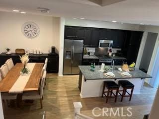 kitchen with stainless steel microwave, a kitchen island with sink, fridge with ice dispenser, dark cabinetry, and a kitchen bar