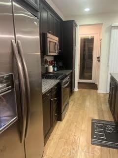 kitchen with light wood finished floors, light stone counters, stainless steel appliances, and dark cabinets