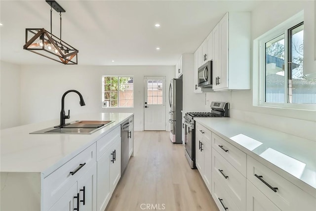 kitchen with pendant lighting, appliances with stainless steel finishes, sink, white cabinets, and light hardwood / wood-style floors