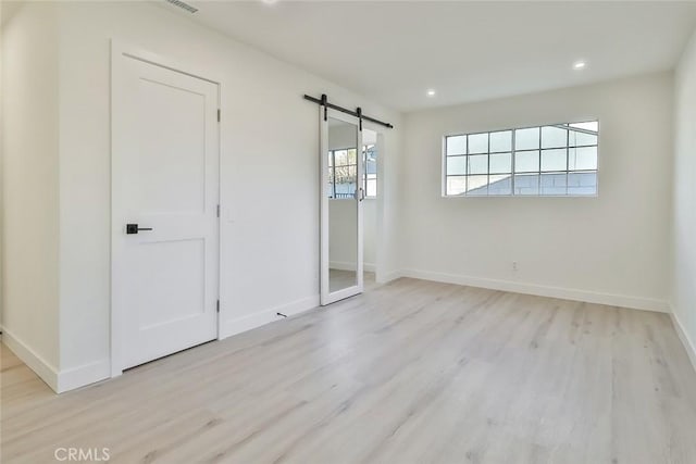 unfurnished bedroom featuring a closet, a barn door, and light hardwood / wood-style floors