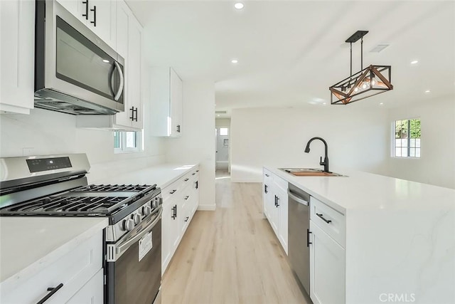 kitchen featuring light hardwood / wood-style floors, white cabinetry, sink, pendant lighting, and stainless steel appliances