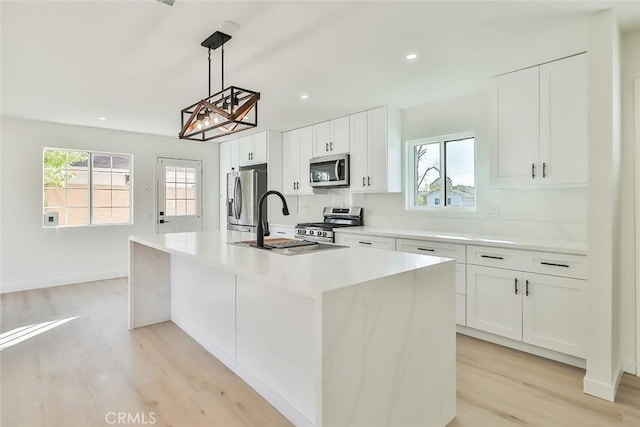 kitchen with white cabinets, light wood-type flooring, pendant lighting, stainless steel appliances, and a center island with sink