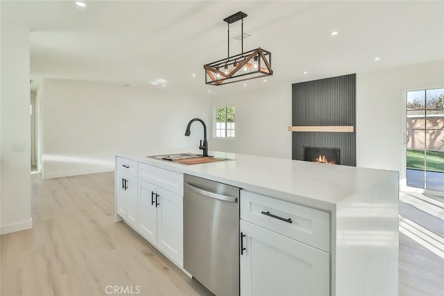 kitchen featuring white cabinetry, a kitchen island with sink, stainless steel dishwasher, sink, and decorative light fixtures