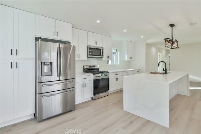 kitchen with an island with sink, white cabinets, hanging light fixtures, and stainless steel appliances