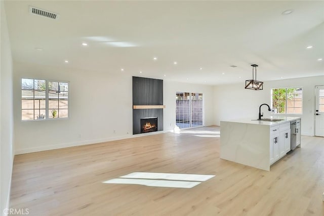 kitchen with a kitchen island with sink, stainless steel dishwasher, white cabinets, decorative light fixtures, and sink