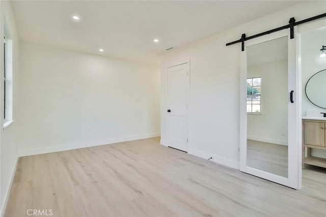 unfurnished bedroom featuring light hardwood / wood-style floors, a closet, ensuite bath, and a barn door