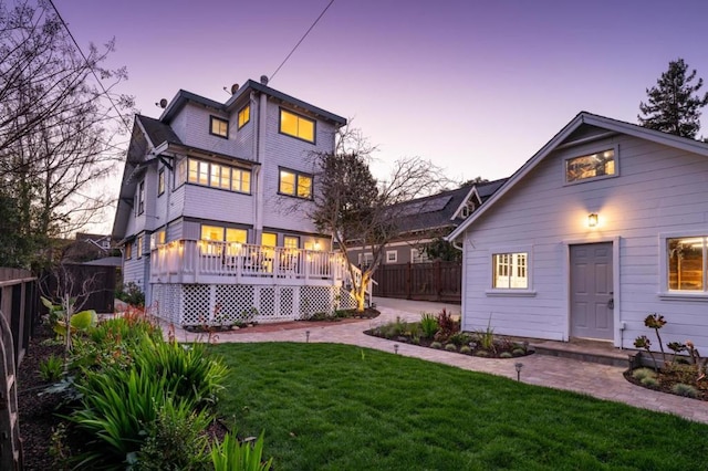 back house at dusk with a wooden deck and a yard