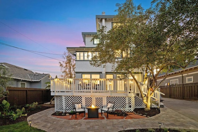 back house at dusk with a wooden deck, a patio, and a fire pit