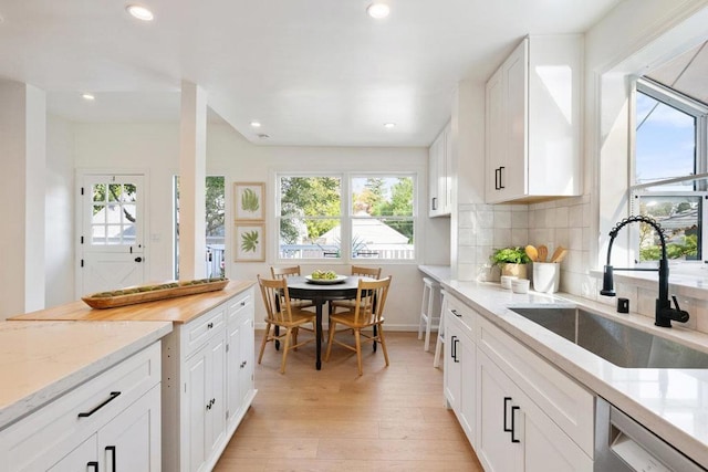 kitchen featuring sink, light hardwood / wood-style flooring, white cabinetry, backsplash, and stainless steel dishwasher