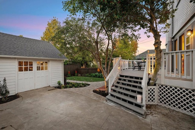 patio terrace at dusk with a garage, a wooden deck, and an outbuilding