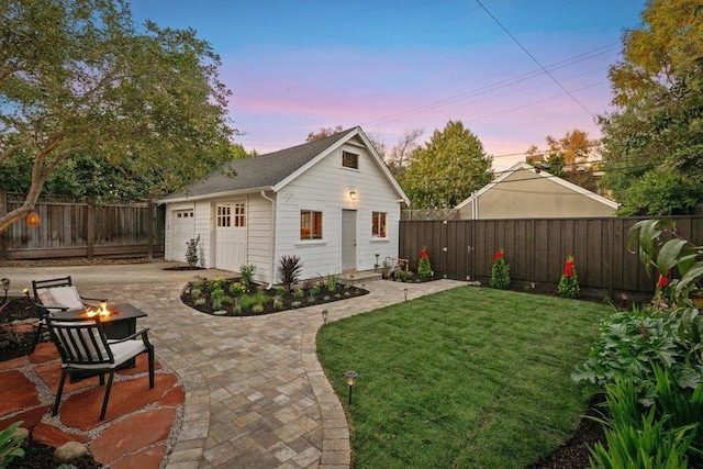 back house at dusk featuring a garage, a yard, an outdoor structure, a fire pit, and a patio