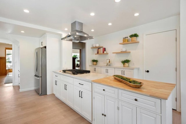 kitchen with wooden counters, appliances with stainless steel finishes, white cabinetry, island range hood, and light wood-type flooring