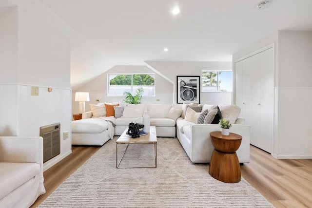 living room with lofted ceiling, heating unit, and light wood-type flooring