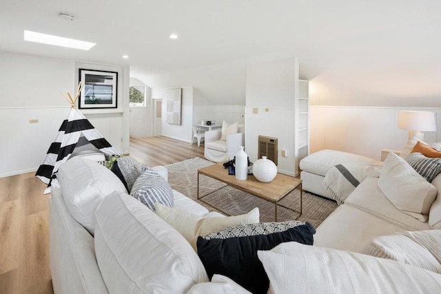 living room featuring lofted ceiling with skylight, heating unit, and light hardwood / wood-style flooring