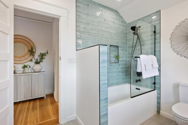 bathroom featuring tile patterned flooring, tiled shower / bath, lofted ceiling, and toilet