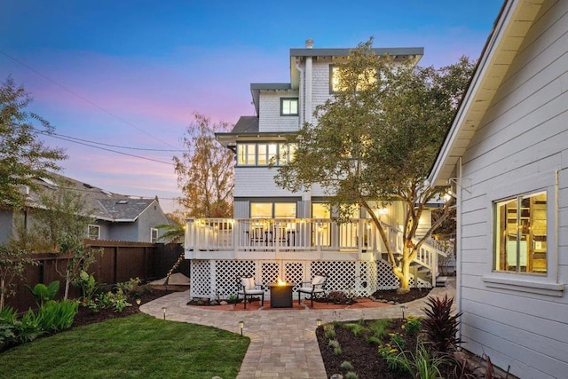 back house at dusk with a patio area, a lawn, and a deck