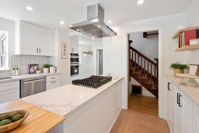 kitchen with white cabinetry, island exhaust hood, stainless steel appliances, and light hardwood / wood-style flooring